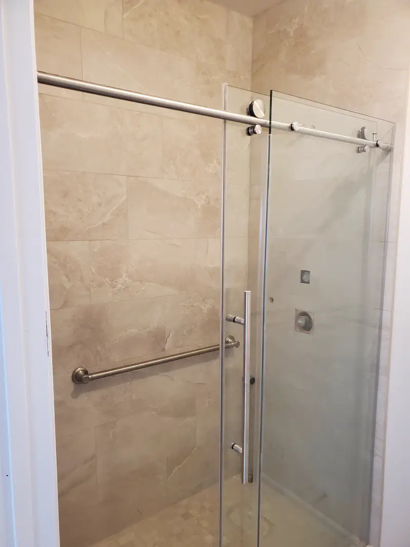 Finished walk-in shower with large marble-look tile, a frameless sliding glass door and a grab bar